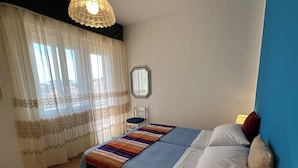Un dormitorio con una cama, una mesita de noche con lámpara, una silla y una ventana con cortinas.
