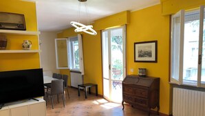 A living room with a television, a dining table with chairs, a sofa, a wooden cabinet, and a patterned rug. - Gian House - centro città (Rimini)