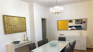 A modern dining area with a glass table, black upholstered chairs, a chandelier, and a decorative painting. - Gian House - centro città (Rimini)