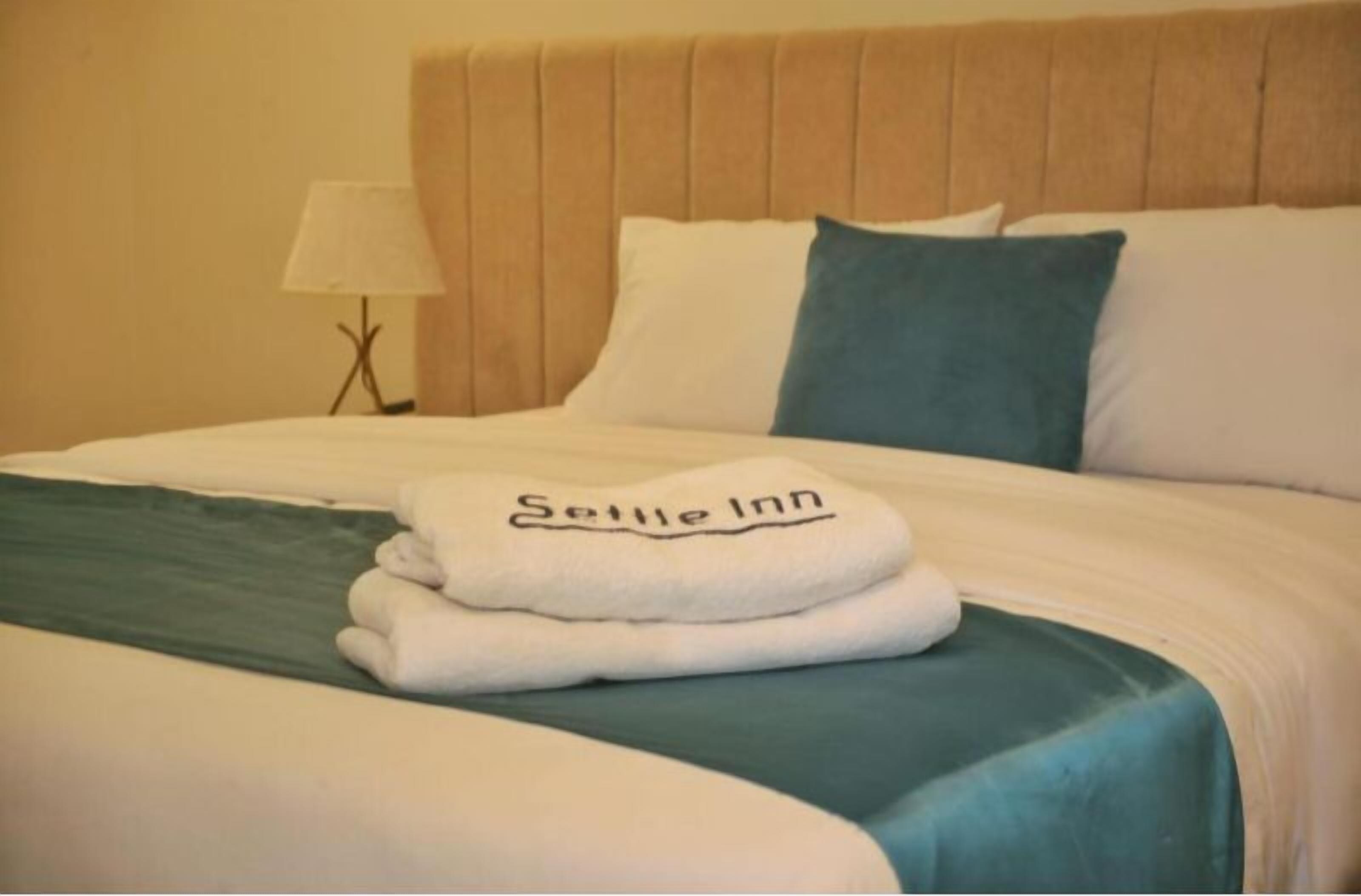 Una cama bien tendida con una toalla blanca doblada y una almohada con la inscripción 'Selle Inn'.