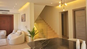 A modern living room with a curved sofa, a marble coffee table, and a staircase with glass railings. - Settle Inn Cairo Festival City Villa (New Cairo)