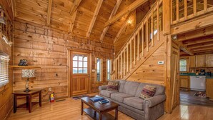 A log cabin interior with a wooden staircase, a sofa, a coffee table, and a kitchen area. - Peace And Quiet With Incredible Views (PIGEON FORGE)