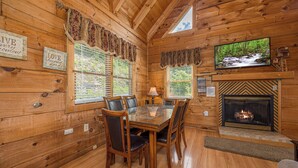 A wooden cabin interior with a dining area, fireplace, and a television mounted above the fireplace. - Peace And Quiet With Incredible Views (PIGEON FORGE)