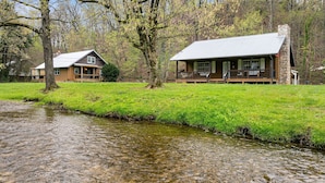 A cabin with a stone chimney, a porch, and a grassy area beside a stream. - Creekside Haven equals a Heavenly Escape (PIGEON FORGE)