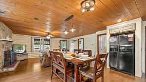A spacious dining area with a wooden table and chairs, a stone fireplace, and a black refrigerator. - Creekside Haven equals a Heavenly Escape (PIGEON FORGE)