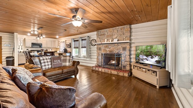 A cozy cabin interior with a stone fireplace, leather sofas, wooden floors, and a television. - Creekside Haven equals a Heavenly Escape (PIGEON FORGE)