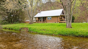 A cabin with a porch, a stone chimney, and a river in front.