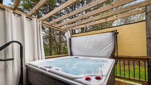 A hot tub with two glasses of red wine, a step leading up to it, and a wooden deck.