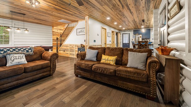 A rustic interior with wooden ceilings, a staircase, a living area with leather sofas, and a kitchen area.