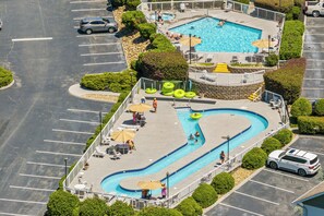 A swimming pool with a winding design, surrounded by lounge chairs and umbrellas, with a parking area visible in the foreground.