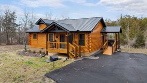 A log cabin with a porch, a covered entryway, and a grill outside.