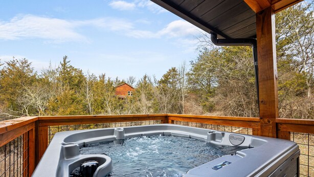 A hot tub on a wooden deck with a view of trees and a house in the background.