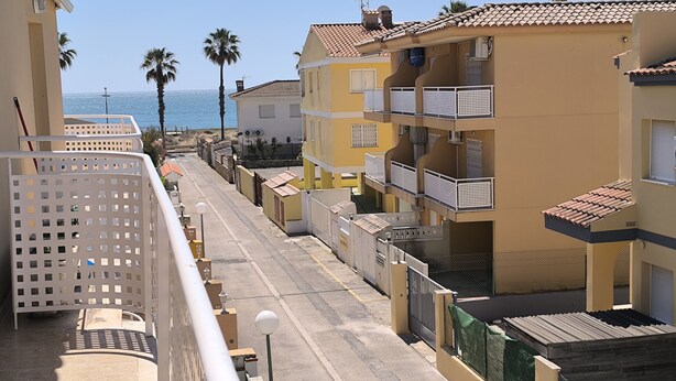 Une rue résidentielle bordée d’immeubles, avec un ciel dégagé et une vue sur la mer.
