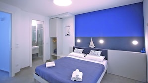 A modern bedroom with a bed, bedside tables, a wardrobe, and a bathroom visible through an open door. - Mandolino Apartment - Two Bedroom Apartment, Sleeps 5 (Syracuse)