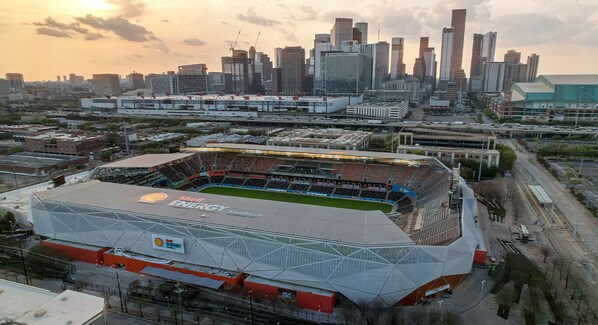 Un estadio con el logotipo de Shell Energy, rodeado por un paisaje urbano con edificios altos y un cielo al atardecer.
