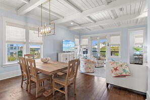 A spacious room with a wooden dining table, chairs, a sofa, and a television.