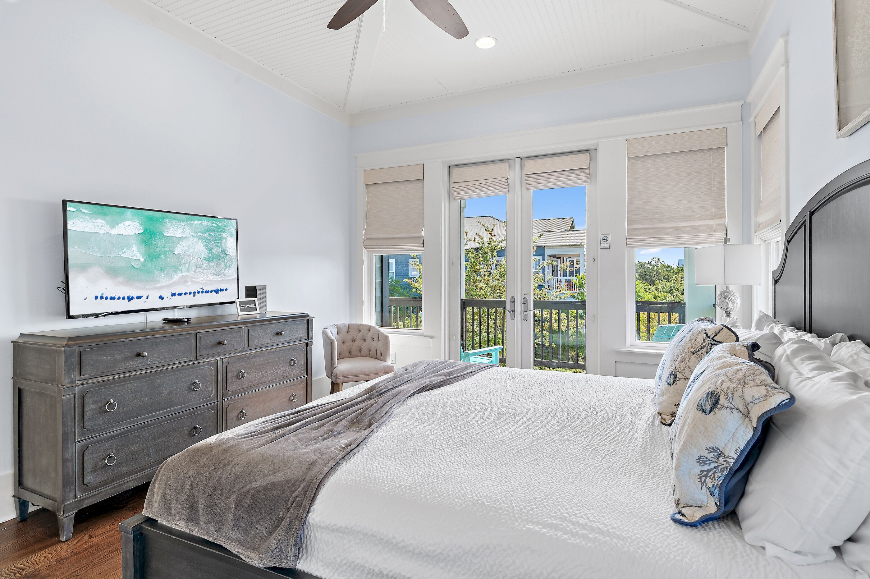 A bedroom with a bed, dresser, TV, and large windows.