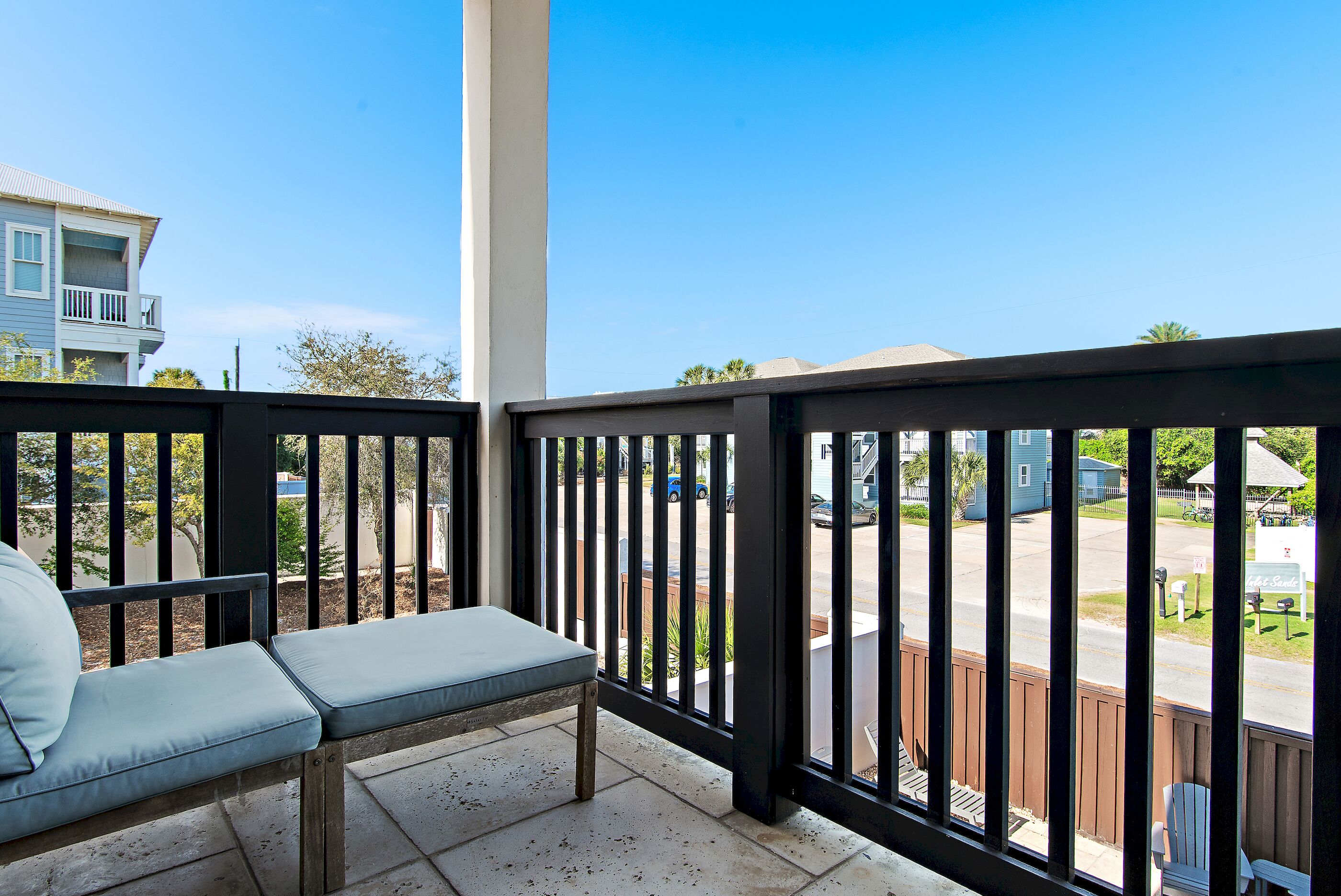 A balcony with a cushioned bench, a railing, and a view of a residential street.