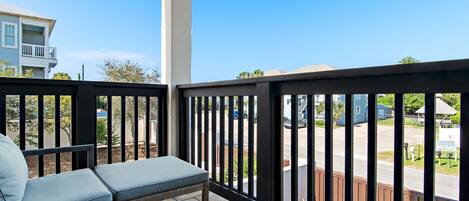 A balcony with a cushioned bench, a railing, and a view of a residential street.