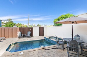 Una piscina con hidromasaje, mobiliario exterior y una sombrilla.