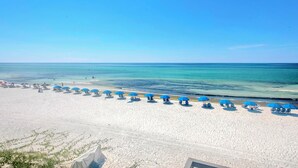 Ein Strand mit Reihen aus blauen Sonnenschirmen und weißen Liegestühlen.