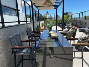 Eine Dachterrasse mit einem langen Tisch, Stühlen, Topfpflanzen und Blick auf die Skyline.