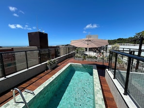 Ein Pool auf dem Dach mit Blick auf den Ozean, ein überdachter Sitzbereich und ein Gebäude mit Satellitenschüssel.