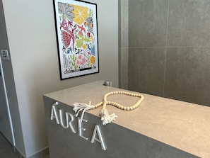 Un mostrador de recepción con una obra enmarcada encima, un collar de cuentas sobre la encimera y la palabra 'AREA' en el mostrador.