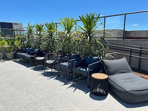 Terraza en la azotea con mobiliario exterior, plantas en macetas y un cielo azul despejado.