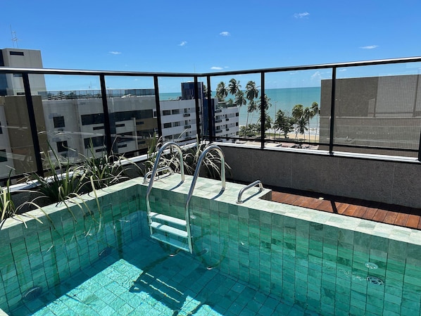 Ein Pool auf dem Dach mit freiem Blick auf das Meer und Palmen.