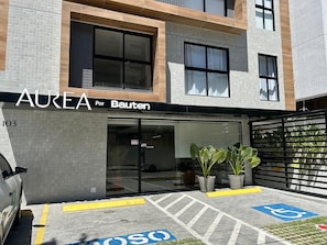 Ein Gebäude mit einer Kachelfassade, ein Schaufenster mit der Aufschrift 'AUREA Por Bauten' und ein Parkbereich mit Stellplatz für Menschen mit Behinderung.