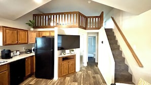 A kitchen with wooden cabinets, a black refrigerator, and a microwave. There is a staircase leading to a loft area with a wooden railing. - Cozy Tiny Home Cabin by Hot Springs, Zip Line, Golf! (Ririe)