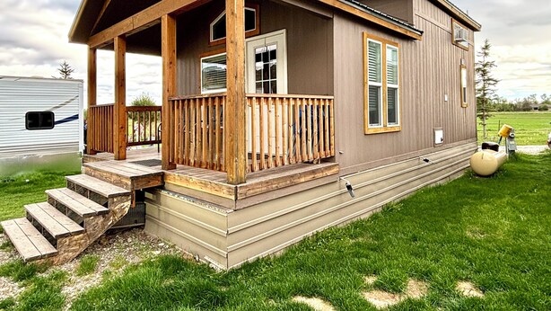 A two-story house with a wooden porch and a small deck, surrounded by a grassy yard. - Cozy Tiny Home Cabin by Hot Springs, Zip Line, Golf! (Ririe)