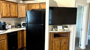 A kitchen with wooden cabinets, a black refrigerator, a microwave, and a built-in TV. - Cozy Tiny Home Cabin by Hot Springs, Zip Line, Golf! (Ririe)