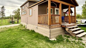 A two-story cabin with a wooden porch and a covered front entrance. - Cozy Tiny Home Cabin by Hot Springs, Zip Line, Golf! (Ririe)