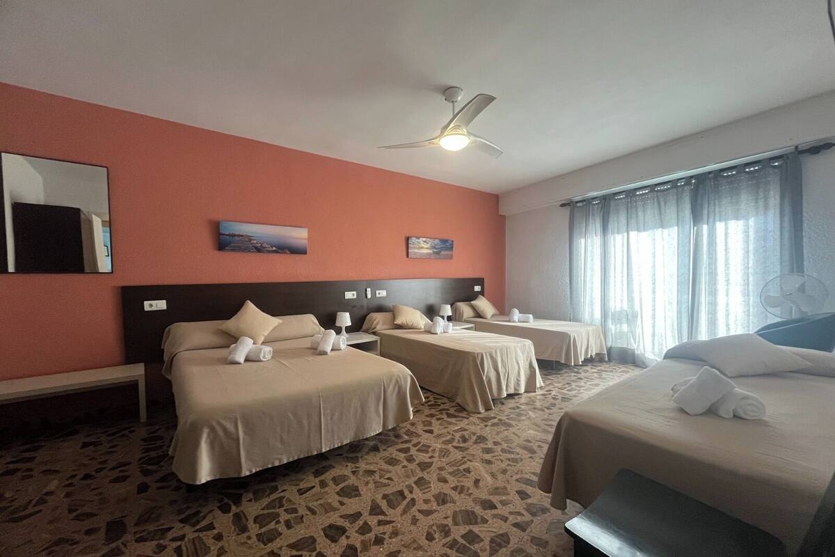 Ein Hotelzimmer mit zwei Betten, einem Deckenventilator, Kunstwerken an den Wänden und einem großen Fenster mit Vorhängen.