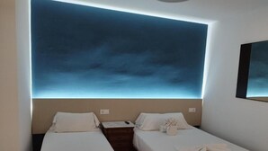 A hotel room with two beds, a nightstand, a wall-mounted TV, and a ceiling light.