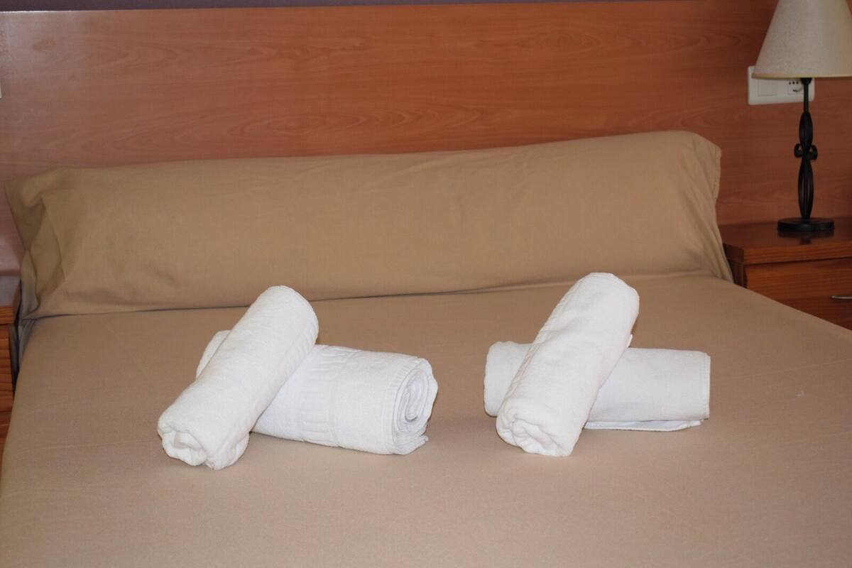 Ein Bett mit zwei gerollten weißen Handtüchern und einem hölzernen Kopfteil.