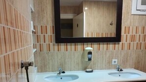 A bathroom with two sinks, a urinal, a mirror, and a soap dispenser.