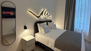 A modern bedroom with a large bed, a bedside table, a wall-mounted mirror, and a decorative light fixture. - Hotel Eleven (Sarajevo)