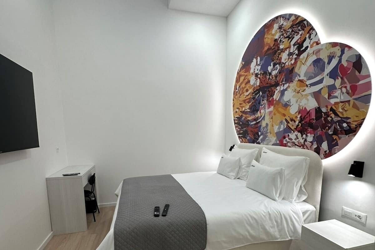 A modern bedroom with a large bed, a desk, and a unique wall art piece.