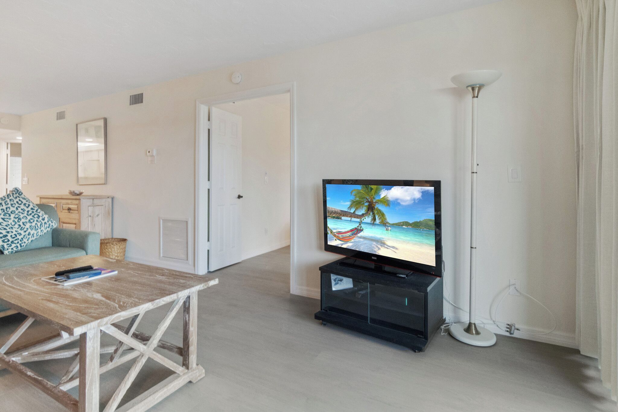 Un salon avec un téléviseur diffusant une scène de plage, une table basse en bois, un canapé et un lampadaire.