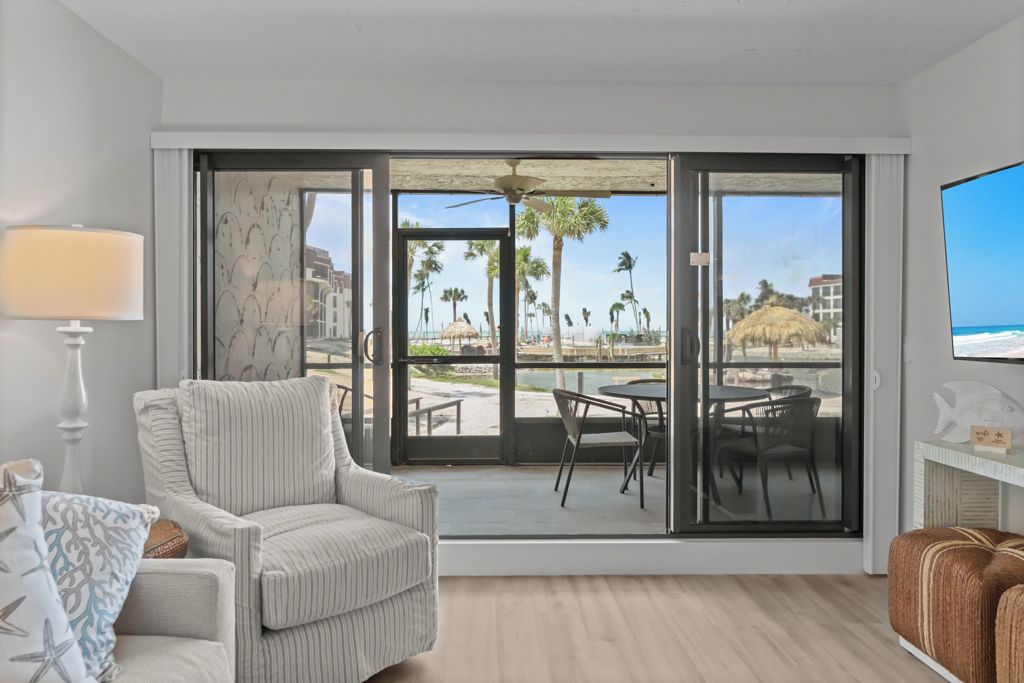 A room with a large sliding glass door leading to a balcony with a view of palm trees and the beach.