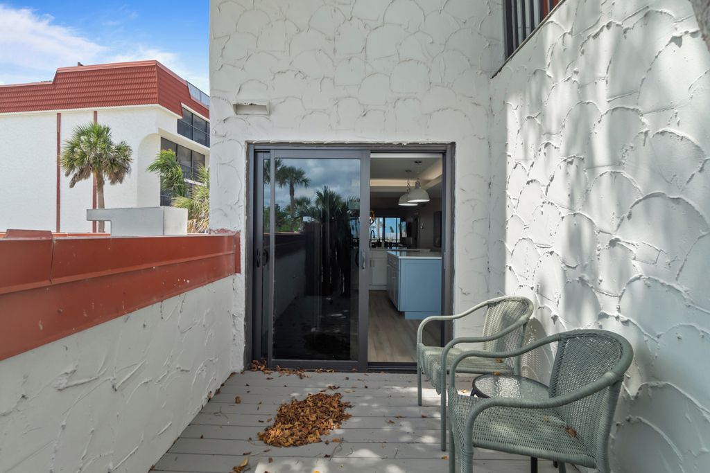 Un petit espace patio avec deux chaises en osier, une porte-fenêtre coulissante donnant sur une cuisine et un mur blanc à texture.