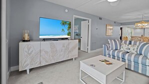 A living room with a large flat-screen TV, a white coffee table, a striped sofa, and a ceiling fan. - Island Bliss Awaits: Spacious 2BR Pointe Santo Condo with Tropical Views (Sanibel)