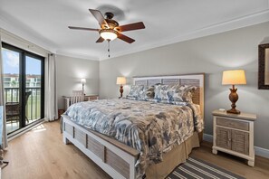 Un dormitorio con cama, dos mesitas de noche, ventilador de techo y vistas a través de un gran ventanal corredizo.