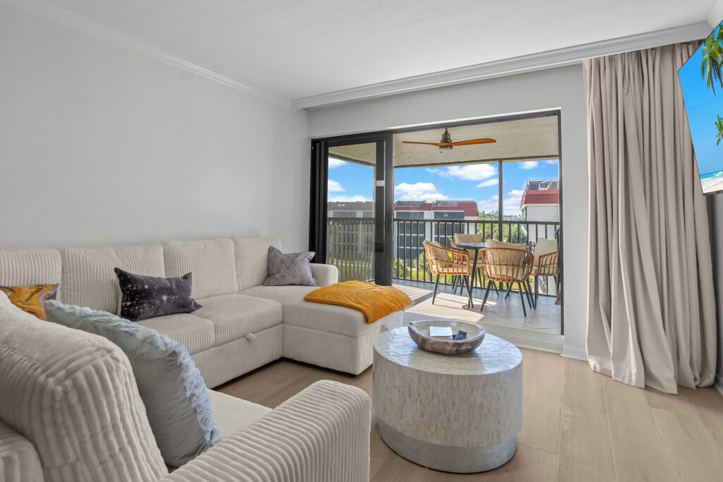 Un salon moderne avec un canapé d’angle, une table basse ronde et un balcon aménagé avec du mobilier d’extérieur.