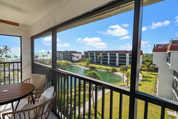A balcony with wicker furniture, a view of a golf course, and a building with a red roof.
