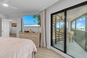 Un dormitorio con una televisión grande, un balcón con vista a la playa y un aparador de mimbre.