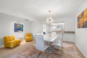 A modern dining area with a white table and chairs, a yellow sofa, and a large painting of a sea turtle.